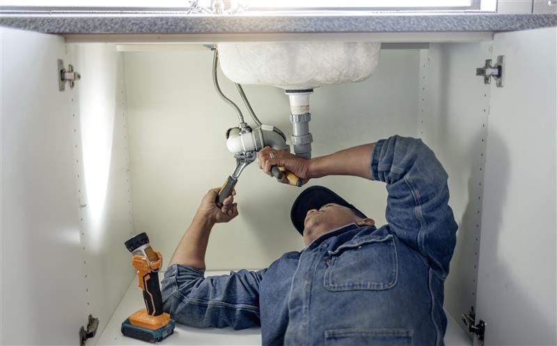 Plumber repairing pipes beneath a bathroom sink in Boca Raton