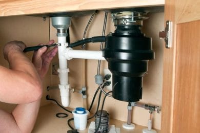 Plumber repairing a garbage disposal beneath a kitchen sink in Boca Raton