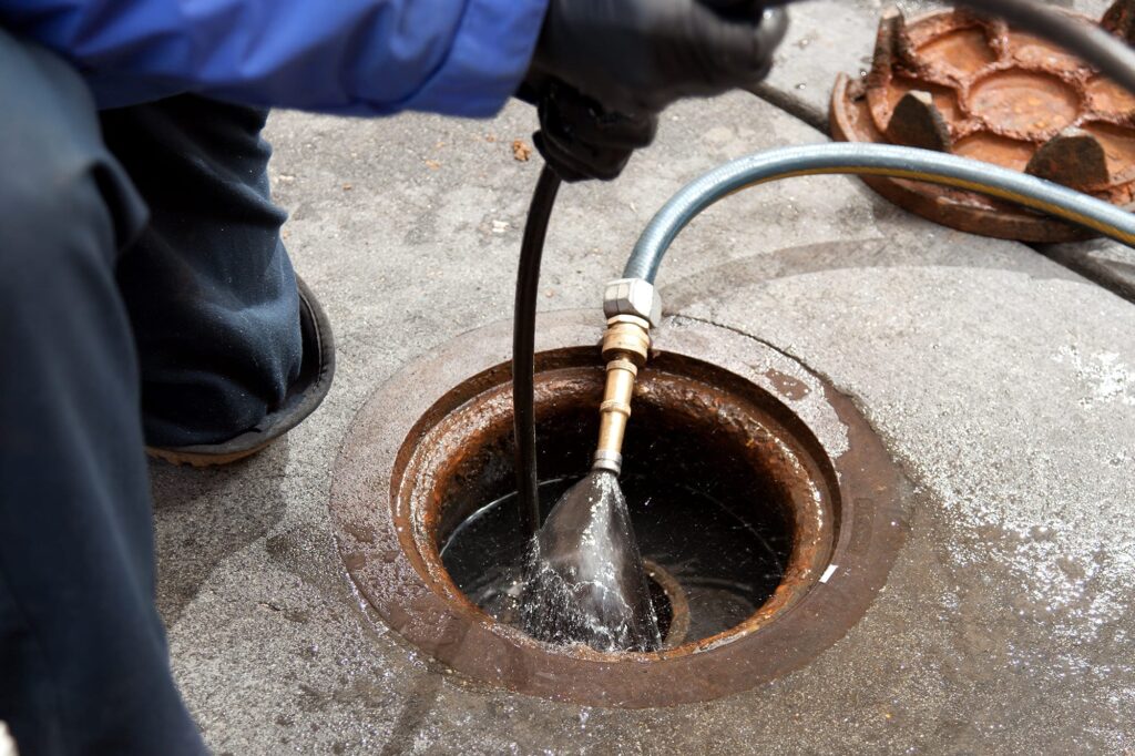 Plumber hydro jetting a sewer line through a manhole in Boca Raton