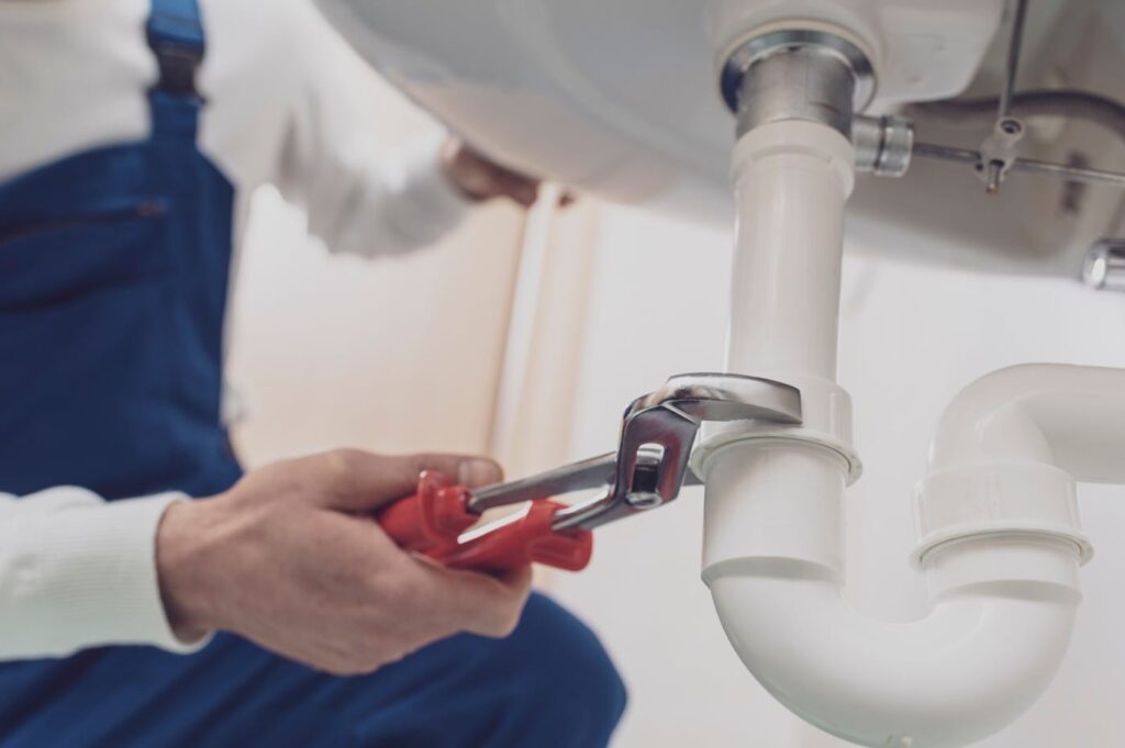 Plumber repairing a white drain pipe beneath a sink in Boca Raton