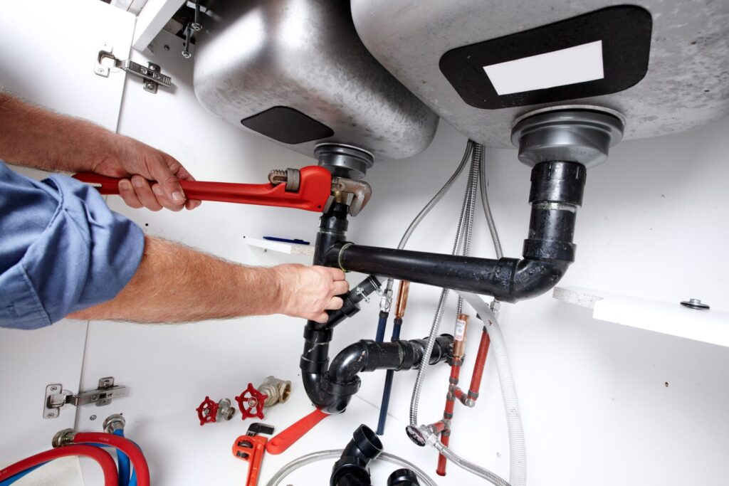 Plumber repairing drain pipes beneath a kitchen sink in Boca Raton